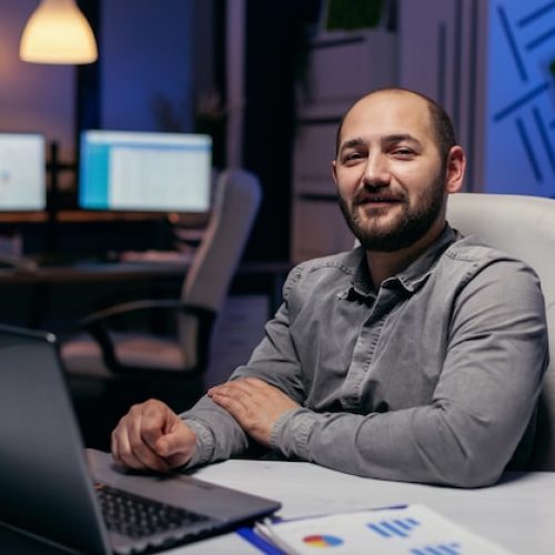 portrait-freelancer-looking-camera-sitting-desk-with-charts-smart-businessman-sitting-his-workplace-course-late-night-hours-doing-his-job_482257-10278